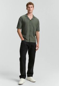 Trumpomis rankovėmis, tekstūruota žalia palaidinė su sagomis priekyje, derinama su juodomis kelnėmis ir baltomis sportbačiais. Paprastas dizainas ir laisvas fasonas.