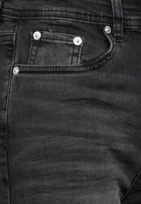 Vaqueros de denim negros con un diseño clásico, estilo de cinco bolsillos, con herrajes en tono plateado y una sutil textura de desvanecimiento.