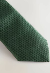 Cravate vert foncé avec un motif tissé texturé comportant de petites formes de diamant. Le matériau semble lisse avec un léger éclat.