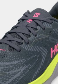 Grijze sportschoen met een gestructureerde bovenkant, zwarte veter, roze branding en een felgele zool. Kenmerkt zich door een gestroomlijnd, modern ontwerp.