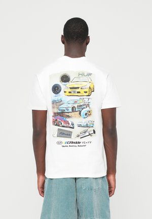 Person trägt ein weißes T-Shirt mit bunten Autodesigns, Geschwindigkeitsmessern und grafischen Darstellungen von Autoteilen auf dem Rücken, kombiniert mit türkisfarbenen Shorts.