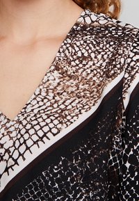 Top a scollo a V caratterizzato da un motivo in pelle di serpente marrone e bianca con dettagli neri, texture liscia e design a vestibilità rilassata.