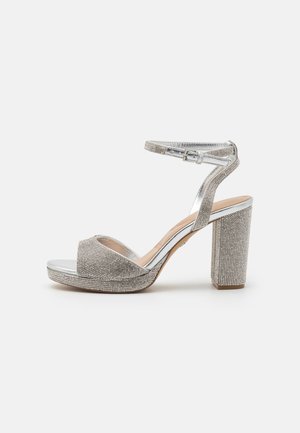 Silver high-heeled sandals with an open toe, sparkling rhinestone embellishments, and a thick block heel. Adjustable ankle strap included.