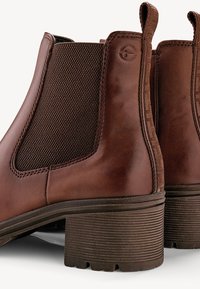 Bottes Chelsea en cuir marron avec des panneaux élastiques texturés sur les côtés, des talons nervurés et un accent subtil à motif à l'arrière.