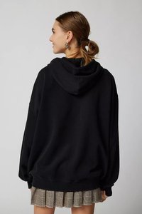 Black oversized hoodie with a drawstring hood, ribbed cuffs, and a loose fit, worn over a patterned pleated skirt.