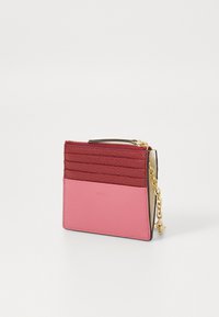 Portafoglio in pelle rosa con scomparti per carte rossi, zip dorata e catena. Presenta il nome del marchio impresso, una texture liscia e un design a colori a contrasto.