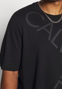 Czarny t-shirt z krótkim rękawem wykonany z bawełny o gładkiej fakturze, z dużym, subtelnym nadrukiem graficznym "CAL" oraz okrągłym dekoltem.