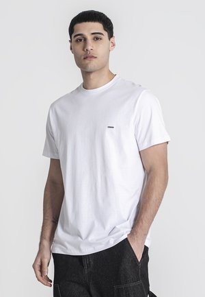 Camiseta de algodón blanca con cuello redondo y mangas cortas, que presenta un pequeño logo negro en el lado izquierdo del pecho y un ajuste relajado.