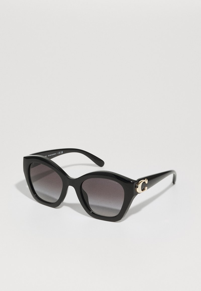 Lunettes de soleil noires avec une forme audacieuse en œil de chat, dotées de verres gris dégradés et d'un accent doré en "G" sur le côté. Fabriquées en plastique brillant.