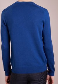 Modrý svetr s kulatým výstřihem a dlouhými rukávy, vyrobený z hladkého materiálu; má ribbované manžety a lem, který z hinten zdůrazňuje přiléhavý siluetu.