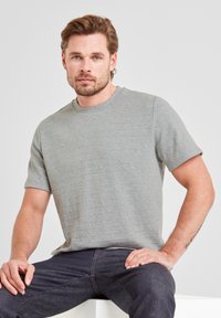Gray short-sleeve T-shirt in a textured knit fabric, featuring a round neckline and a relaxed fit. Worn with dark denim jeans.