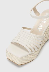 Hvite kilehæler med en teksturert espadrille-base, flere vertikale stropper og et kvadratisk tådesign.