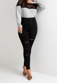 Top grigio a maniche lunghe con sovrapposizione in pizzo nero, abbinato a jeans skinny neri strappati e tacchi con stampa leopardata. Design semplice e moderno.