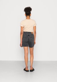 Los pantalones cortos de mezclilla negra descoloridos presentan una cintura alta, bolsillos traseros con detalle de costura y se combinan con una camisa a rayas beige.