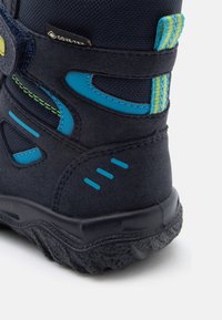 Mørkeblå fjellsko med en teksturert semsket lær og syntetisk overdel. Inkluderer blå og grønne detaljer, et Gore-Tex-merke, og en robust såle.