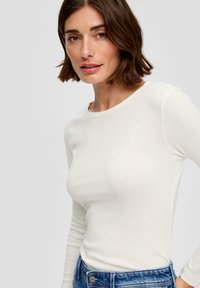 Langsleeve, ronde hals top in zachte witte stof; gladde textuur met een aansluitend ontwerp gecombineerd met blauwe denim jeans.
