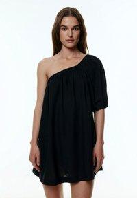Zwarte, one-shoulder jurk met een pofmouw en een gathered halslijn. Zacht, gestructureerd materiaal met een losse, comfortabele pasvorm.