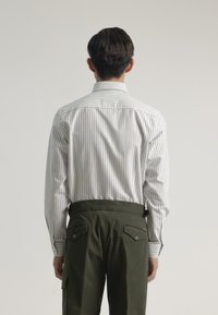 Camisa de manga larga a rayas blancas y grises con cuello, combinada con pantalones verde oliva que tienen dos bolsillos traseros y detalles de botones.