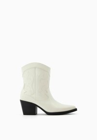Białe skórzane botki za kostkę z szpiczastym czubkiem, zaokrąglonymi przeszyciami i czarnym słupkowym obcasem. Gładka faktura i wzór inspirowany stylem western.