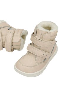 Bottes d’hiver beige pour tout-petits en cuir texturé, fermetures ajustables à double bride et doublure intérieure en polaire blanche douce.