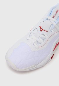 Λευκό αθλητικό παπούτσι με κόκκινο λογότυπο Mizuno, λευκά κορδόνια, επάνω μέρος από δίχτυ και κείμενο "Mizuno Energy" στη σόλα κάτω από απαλό φωτισμό.