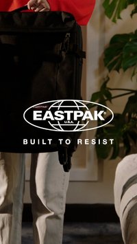 Bolsa Eastpak negra con un diseño estructurado, que presenta un asa resistente y un cierre de cremallera, en un fondo de follaje verde y parte de un interior claro.