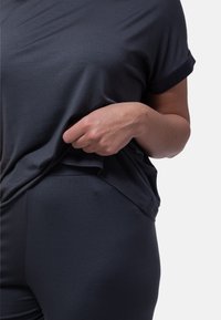 Donkergrijs, kortmouwig, relaxed-fit shirt van zachte stof, gecombineerd met bijpassende strakke broek. Opvallende opgerolde mouwen en een gladde textuur.