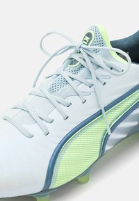 Lyseblå fotballsko med teksturert overdel, grønne detaljer og meshinformasjon. Har snøring og fleksibel såle.