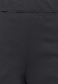 Calças de tecido negro com uma textura suave, apresentando um design simples e um cós. Sem padrões visíveis ou acessórios.