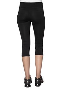 Czarne legginsy capri wykonane z elastycznej tkaniny, o dopasowanym kroju i długości do połowy łydki, w zestawie z czarnymi butami sportowymi.
