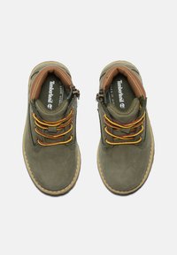 Scarpe in suede verde con dettagli marroni, con lacci gialli e rossi, punta rotonda e suola piatta in gomma per maggiore aderenza.