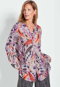 Multikleurige blouse met knopen, featuring bloemen- en abstracte patronen in paars, oranje, rood en zwart op een lichte achtergrond; zachte stof, losse pasvorm.