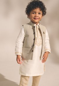 Tenue traditionnelle de couleur claire comprenant un gilet beige à boutons, un kurta blanc orné et un pantalon beige.