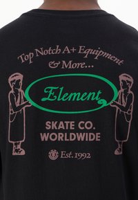Svart bomull T-skjorte med grafisk design med brunt tekst og grønn oval. Inkluderer figurer på begge sider. "Element" logo i midten.