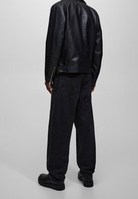 Chaqueta de cuero negra con silueta ajustada y puños con cremallera; combinada con pantalones de mezclilla negros holgados y calzado grueso negro.