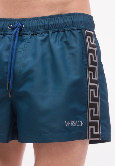 Μπλε μαγιό σορτς με ελαστική μέση, ρυθμιζόμενο κορδόνι και μαύρο πλαϊνό μοτίβο με σχέδιο ελληνικού κλειδιού. Λογότυπο: Versace.