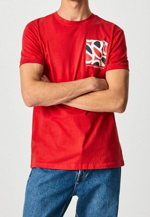 Rød bomuld T-shirt med korte ærmer, rund halsudskæring og et mønstret brystlomme i sort og hvidt mønster.
