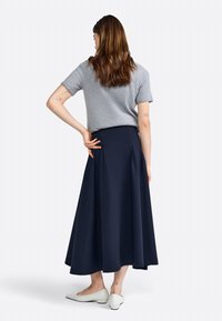 Haut gris à manches courtes associé à une jupe fluide bleu marine. La tenue présente une taille cintrée et un design plissé, complétée par des ballerines blanches.