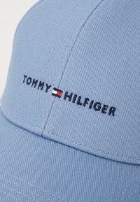 Blauwe pet van katoen twill, met een geborduurd logo in rood, wit en blauw. Stikdetails zijn zichtbaar langs de naad.