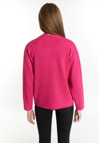 Fuchsia oversized sweater with a textured knit design. Features a round neckline and dropped shoulders, paired with black fitted jeans.