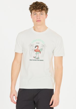 White cotton t-shirt featuring a graphic of a flamingo on a surfboard, surrounded by palm trees, with the text "COWABUNGA DUDE" and "FREE TO RIDE THE WAVES."