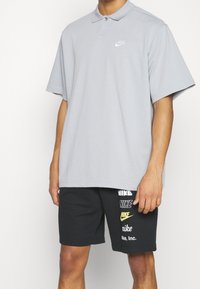 Gray polo shirt with short sleeves featuring a white Nike logo, paired with black shorts displaying multiple Nike logos in white and yellow.