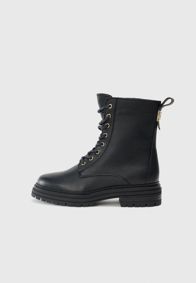 Botas negras de piel hasta el tobillo con un acabado texturizado, con ojales dorados, diseño con cordones y un bucle en la parte trasera. Suela gruesa.