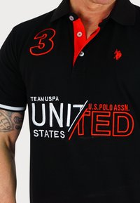Svart polotröja med röd krage och knappar, med broderad vit och röd text, "TEAM USPA UNITED STATES" och ett stort rött nummer "3."
