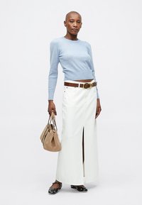 Lys blå genser, hvit denim maxiskjørt med frontspalte, brun lærbelte og en beige håndveske. Svart leilighetssko med detaljer.