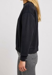 Felpa nera con collo rotondo, tessuto strutturato e polsini a coste. Presenta una vestibilità comoda e dettagli con cuciture visibili.