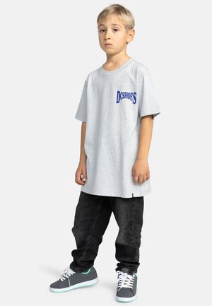 Grijze katoenen t-shirt met blauwe "DC SHOES" logo, gecombineerd met zwarte denim jeans en grijze sneakers met turquoise accenten.