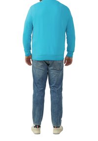 Türkise Sweatshirt mit langen Ärmeln und rundem Halsausschnitt, kombiniert mit hellblauen Jeans und weißen Sneakers mit schwarzen und roten Akzenten.