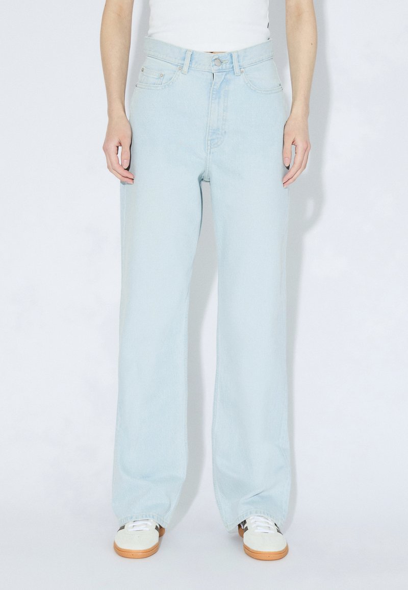 Jasnoniebieskie szerokie spodnie dżinsowe z wysokim stanem, pięcioma kieszeniami i subtelnym blaknięciem, zestawione z białymi trampkami.