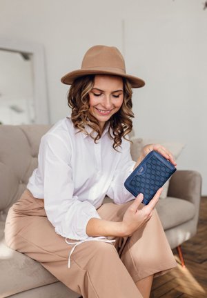 Navy blue wallet with a geometric pattern, textured surface, and silver hardware, held by a person wearing a white blouse and beige pants.